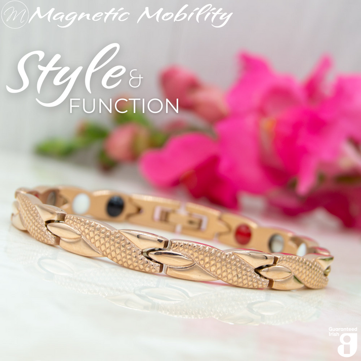 Snapdragon Dawn 4in1 Magnetic Bracelet, rose gold coloured bracelet with snakeskin type designs, designed for pain relief, featuring various therapeutic elements. The bracelet is shown on a reflective surface with a pink flower behind it.