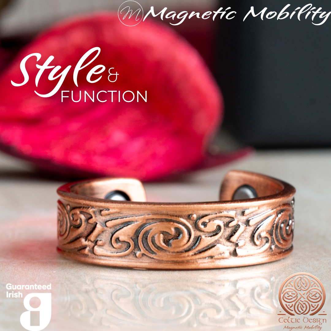 Front view of the Feverfew copper ring by Magnetic Mobility featuring an intricate Irish design. This adjustable ring is designed to be easily worn on arthritic fingers, providing both style and functionality. The image shows the ring in front of a red Christmas decoration.
